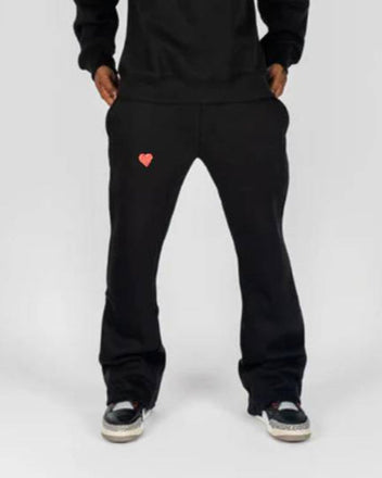 Person wearing a black hoodie and pants with heart designs on a white background