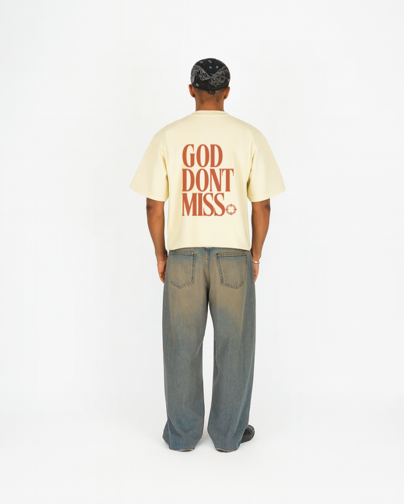 Person wearing a beige t-shirt with 'GOD DON'T MISS' text on the back, standing against a white background.