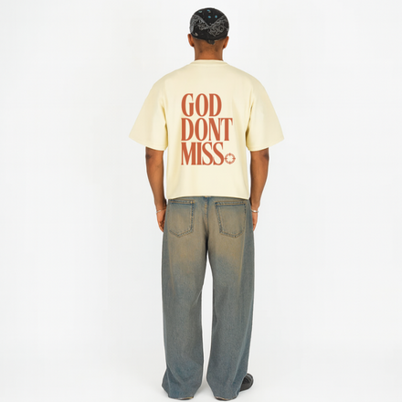 Person wearing a beige t-shirt with 'GOD DON'T MISS' text on the back, standing against a white background.